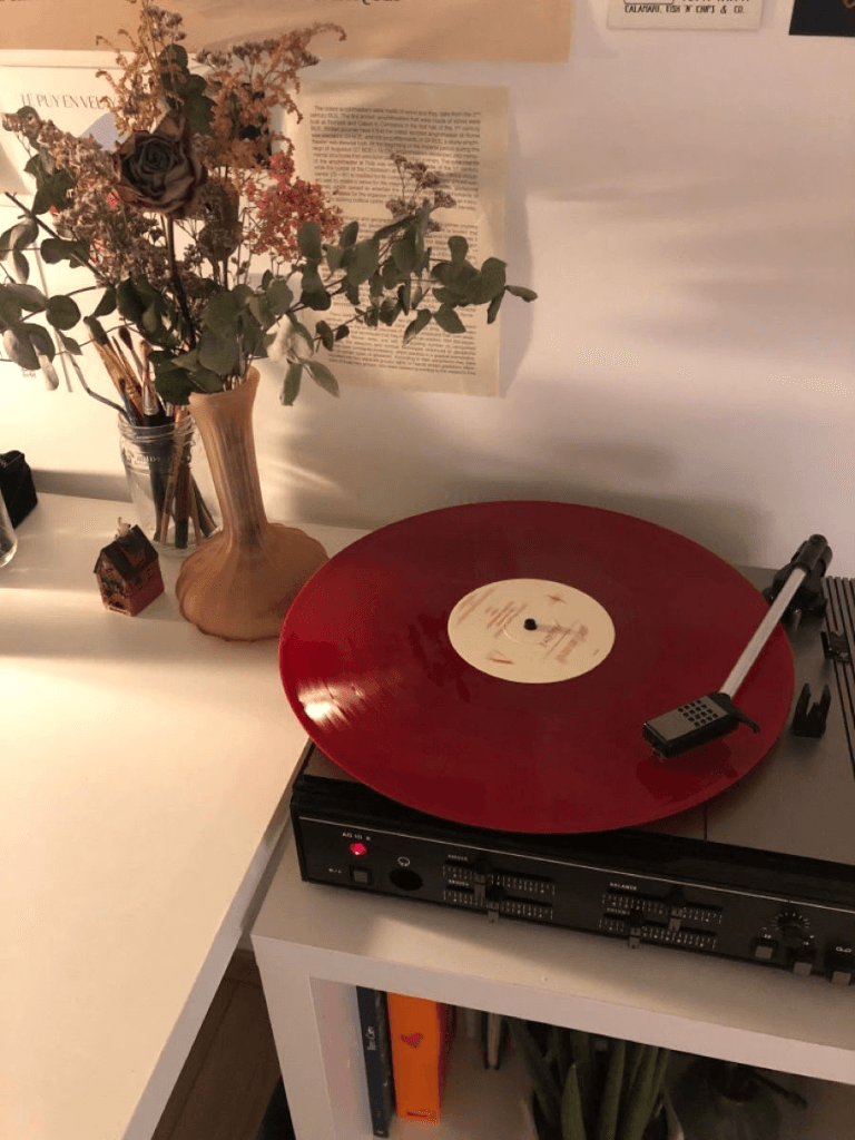 Red vinyl record playing beside a vase of flowers